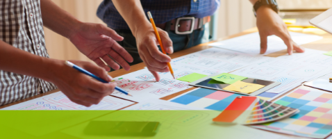 Hands collaborating over design plans and color swatches, symbolizing Creating Customer Value in the Marketing Certificate.