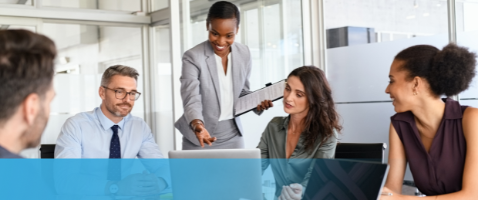 Team collaborating with leader pointing at laptop, representing Strategic Management in Action in the Management Certificate.